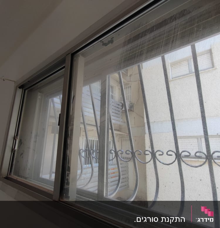 חלון עם מסגרת מתכת וסורגים חיצוניים